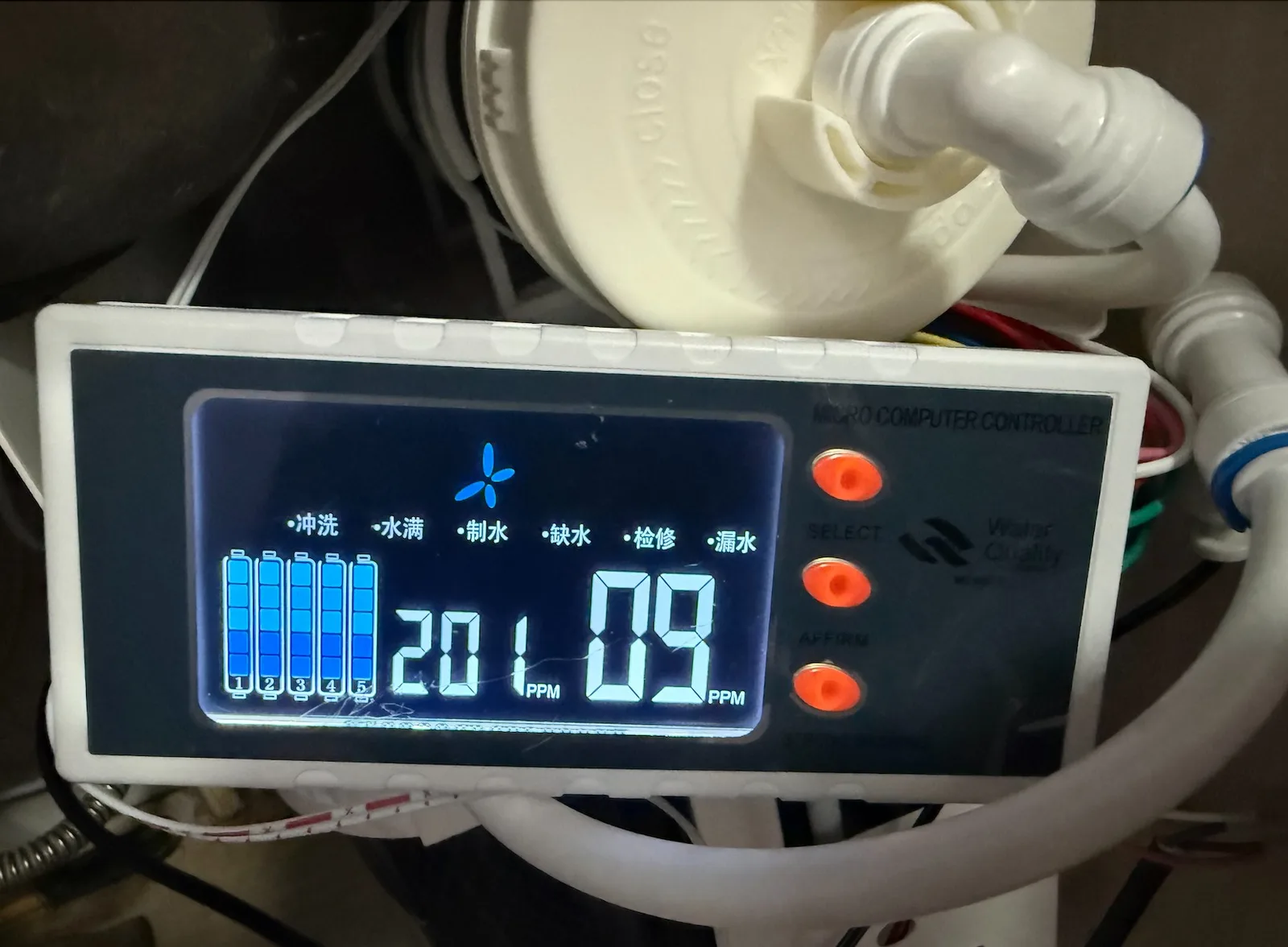 An installed RO controller with an illuminated display and three orange buttons, surrounded by water tubing.